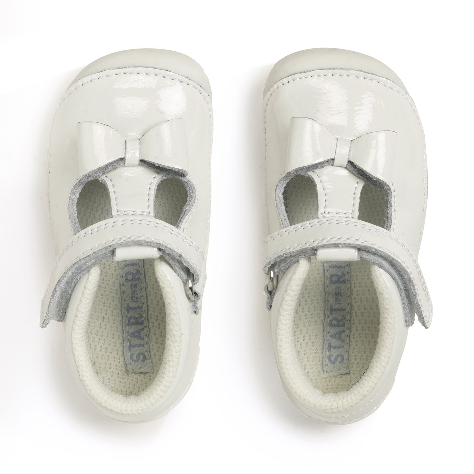 A pair of girls pre-walkers by Start-Rite, style Wiggle, with bow detail, in white patent leather. Toe bumper and velcro fastening. Above view.