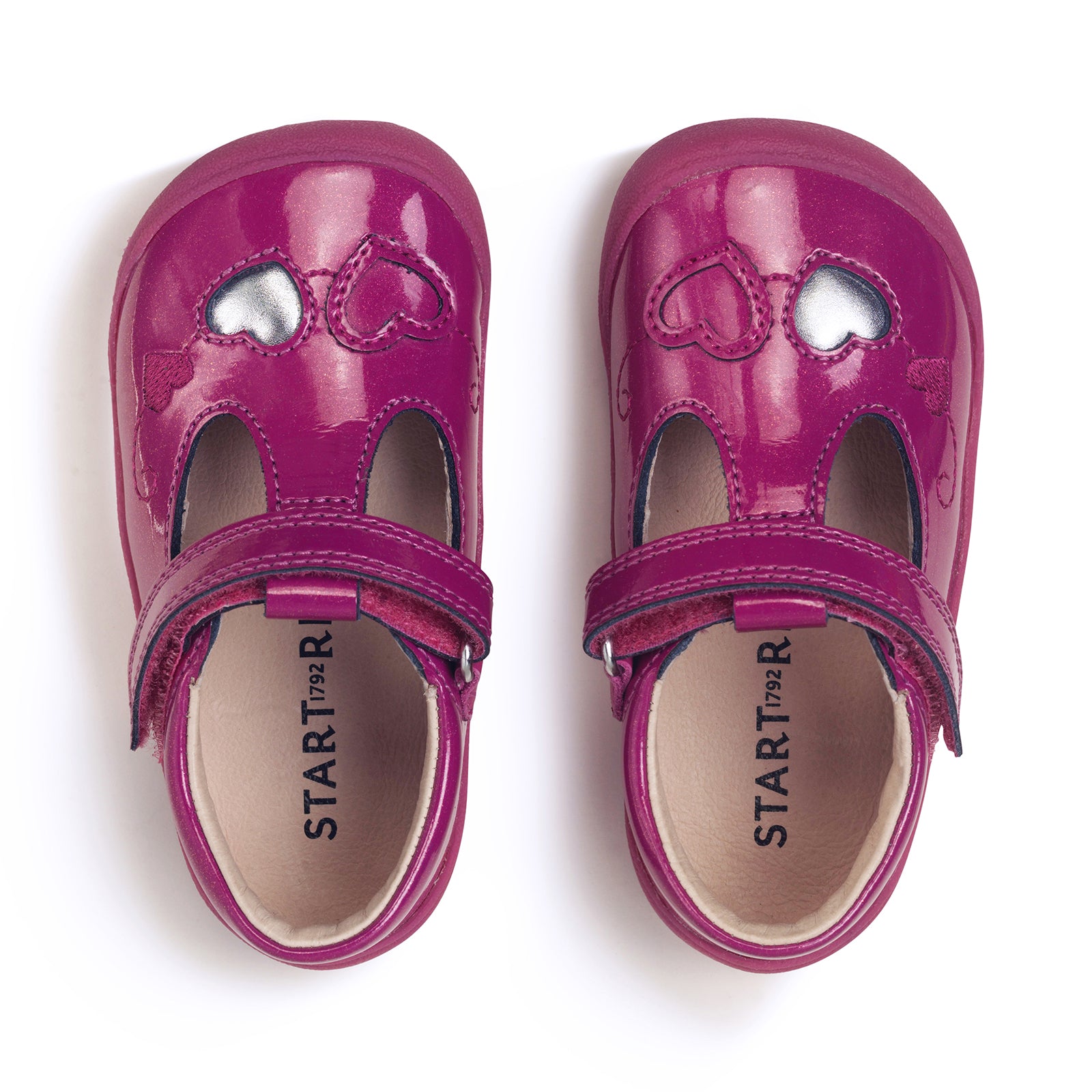 A pair of girls T-Bar shoes by Start-Rite, style Party, in pink glitter leather with pink heart and silver heart detail and velcro fastening. Above view.