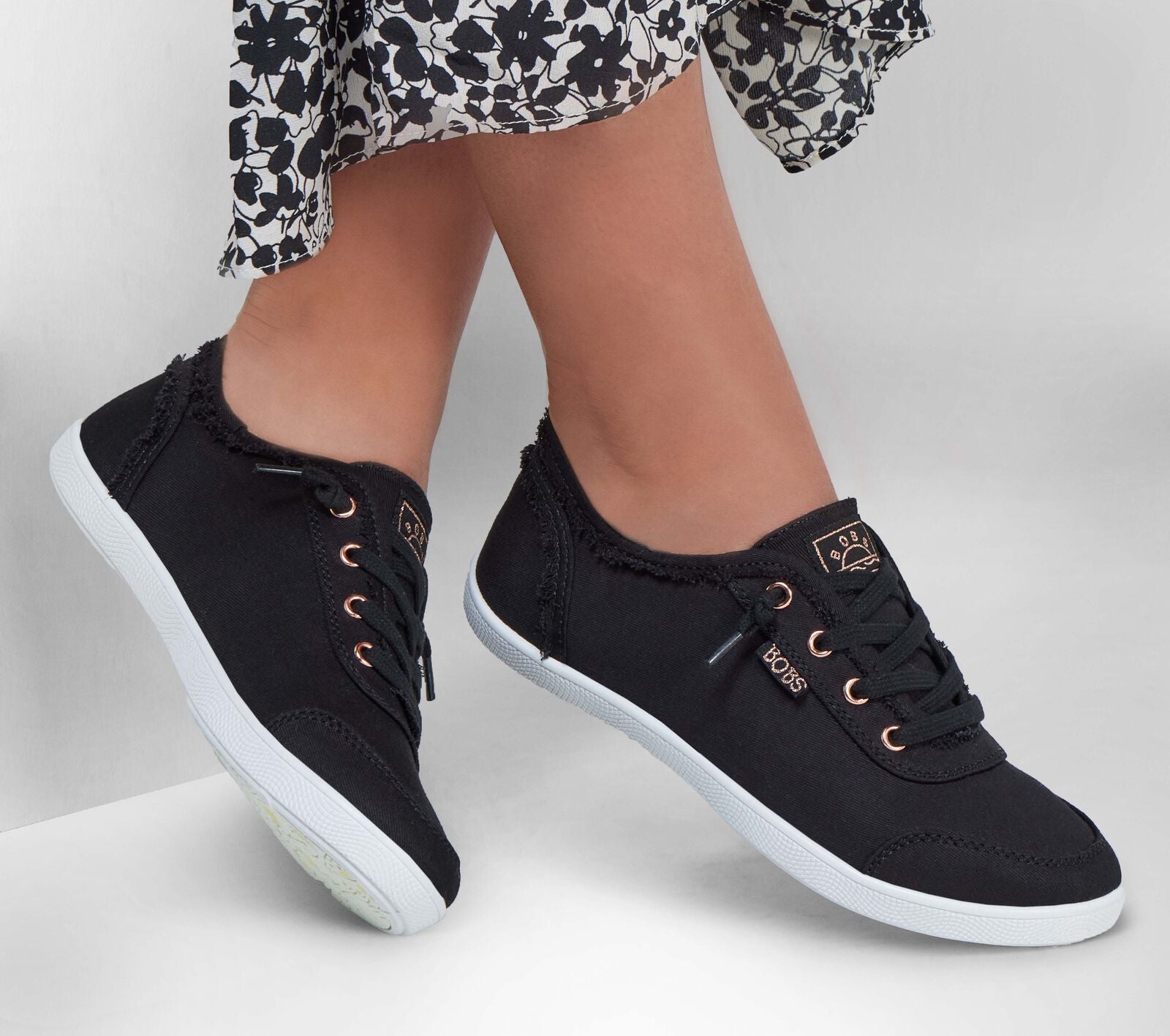 A womens casual shoe by Skechers, style Bobs D'Vine in black canvas, lace fastening. Lifestyle image of lady wearing a pair.