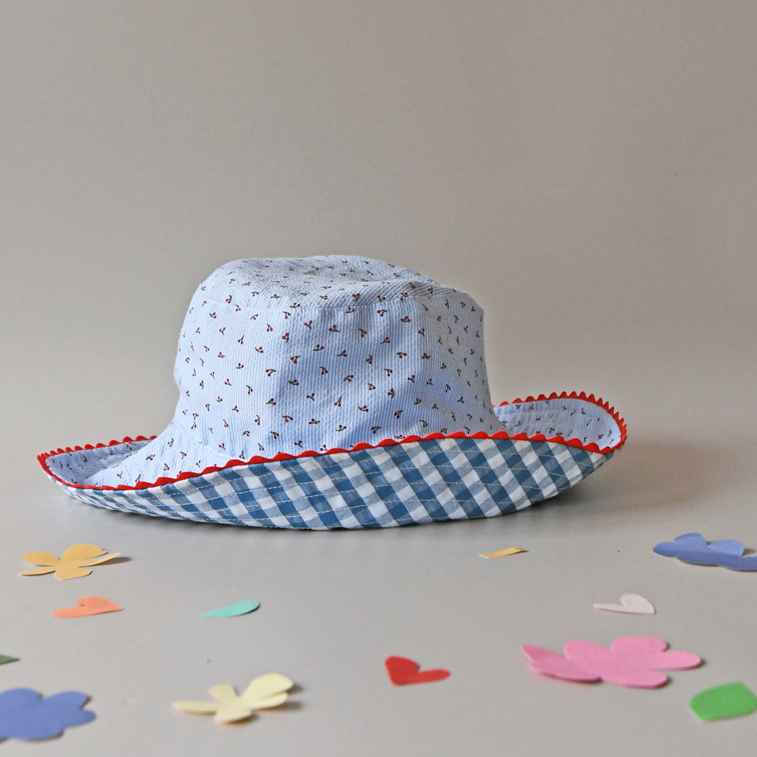 A reversible girls bucket hat by Rockahula, style Cherry Gingham,one side is blue and white stripe cherry print, the other blue and white gingham with cherry embroidery. Front view showing both sides of hat.