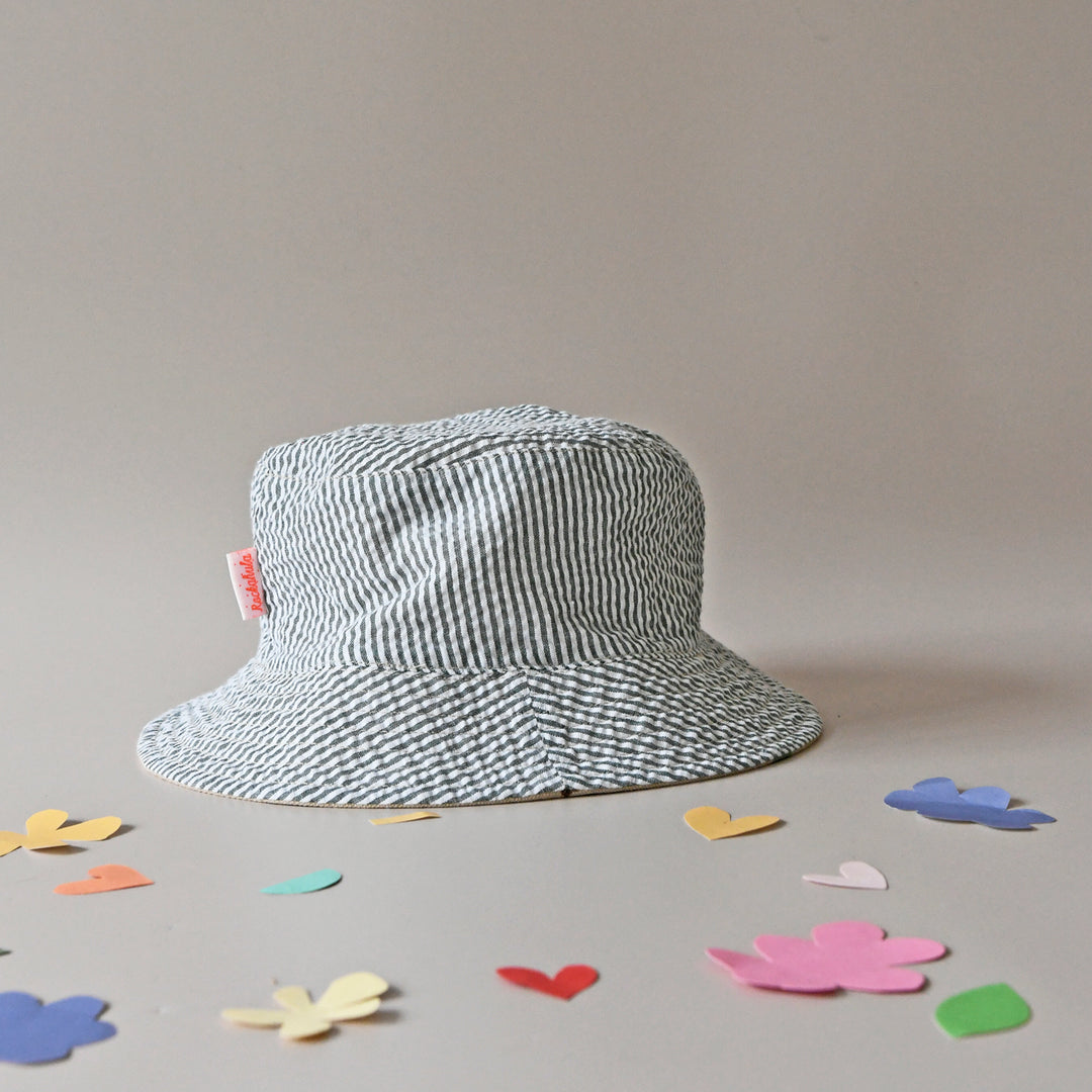 A pair of revirsable children's hats by Rockahula, style Sleepy Sloth, in beige with sleepy sloth print on one side and green stripe print on the other. Front view of green stripe side of hat.