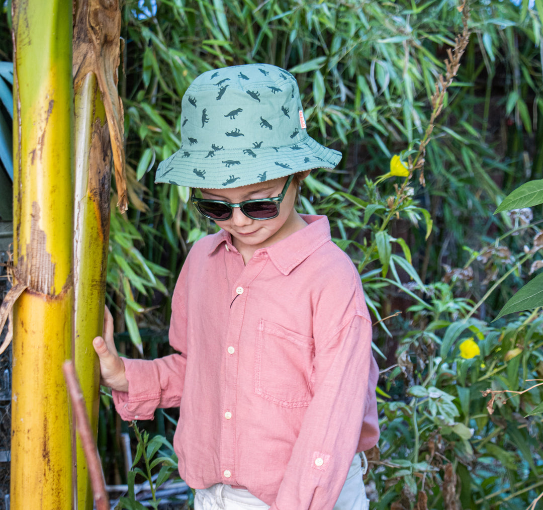 A children's bucket hat by Rockahula, style T-Rex, in green dinosaur print. Front view. Lifestyle image.