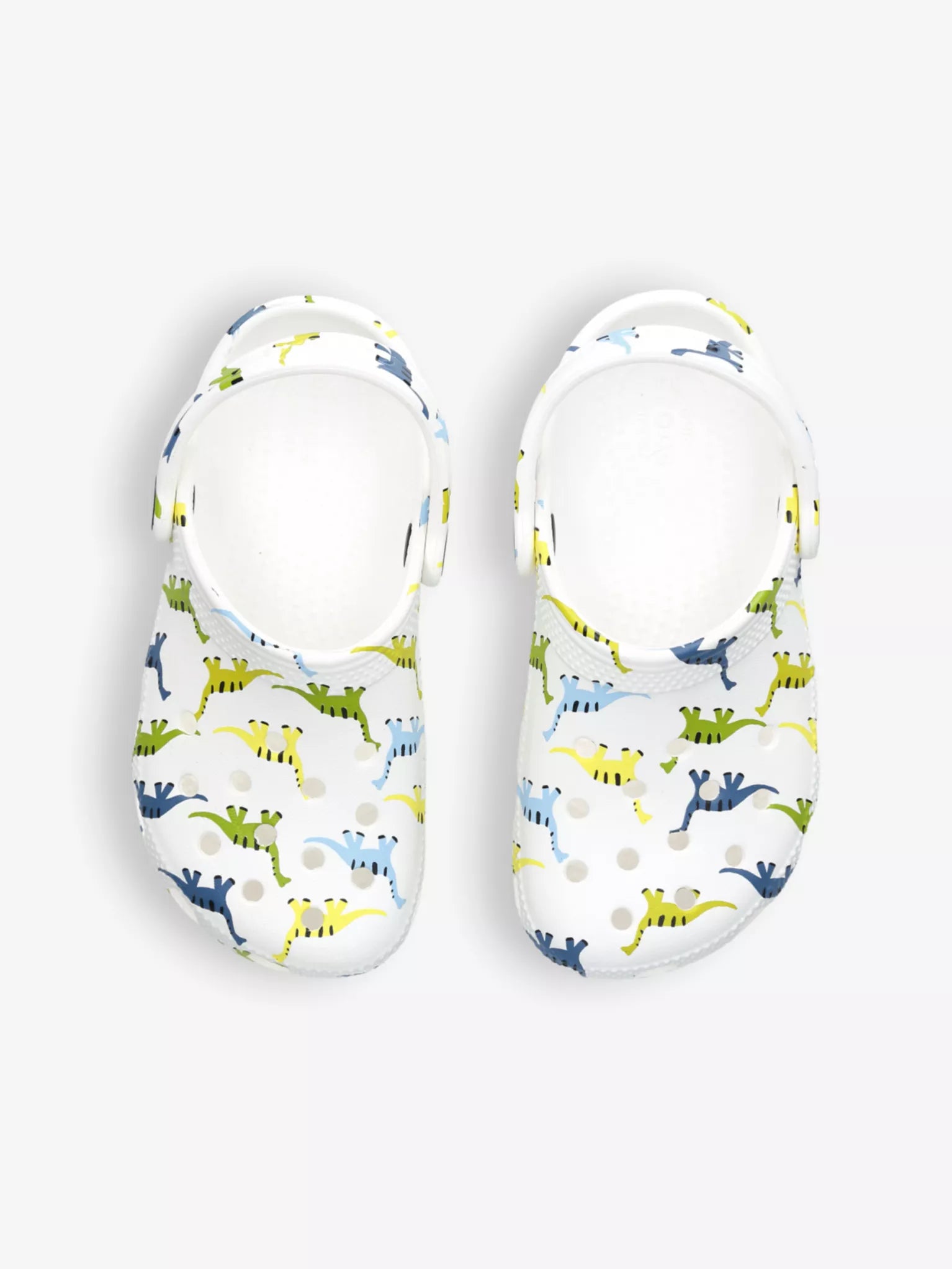 A classic clog by Crocs, style Tod in white with dinosaur print. Above view of a pair.