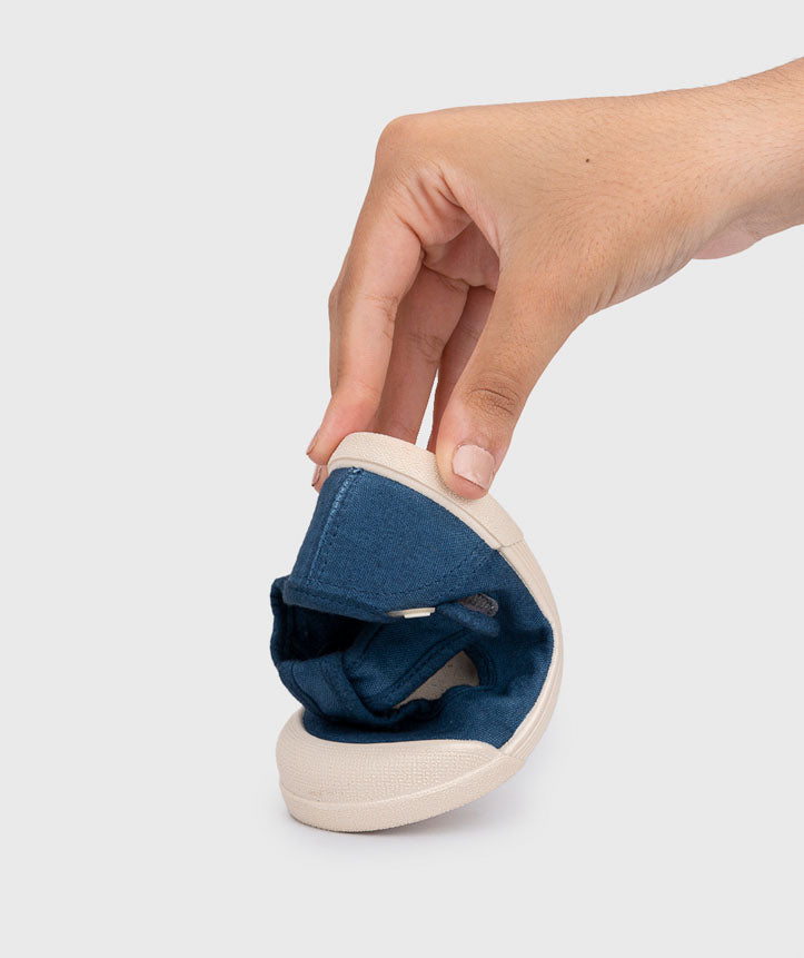 Igor Style Lona Pepito, a T-bar pump in navy with velcro fastening on a cream sole and a toe bumper. Image showing a female hand squishing the shoe.