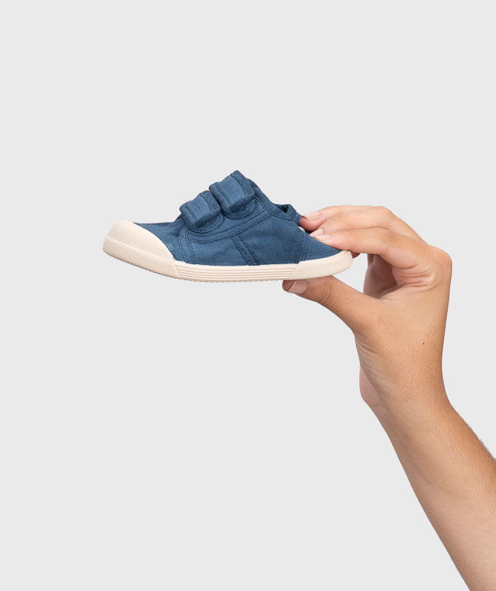 Igor Style Lona Velcro, a double velcro pump in navy with two velcro fastenings on a cream sole and a toe bumper. Image of a female hand squishing the back of the shoe.