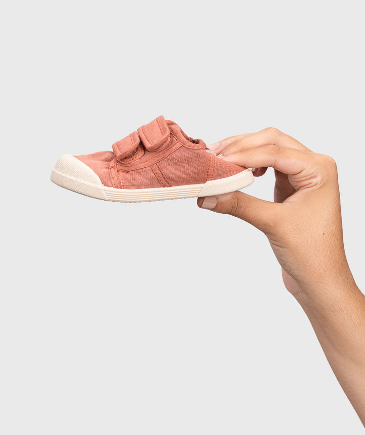 Igor Style Lona Velcro, a double velcro pump in terracotta with two velcro fastenings on a cream sole and a toe bumper. Image showing a female hand squishing the back of the shoe.