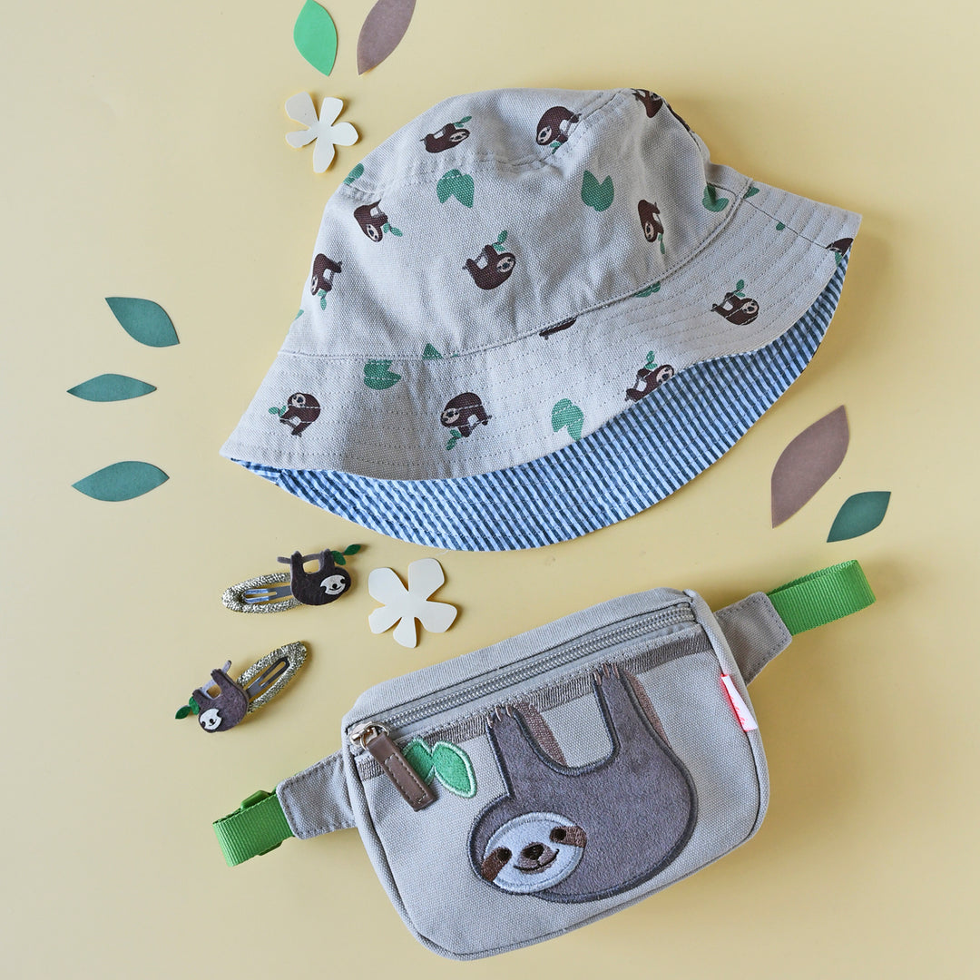 A children's bum bag by Rockahula, style Sleepy Sloth, in beige with sloth print to front and zip fastening. Lifestyle image showing bum bag with matching hat and accessories.