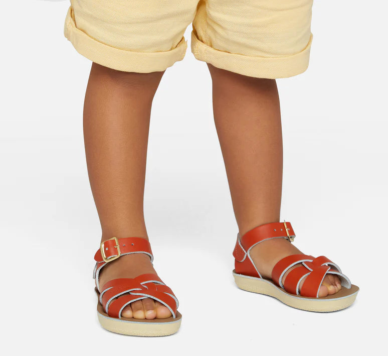 A unisex swimmer design sandal by Salt Water Sandals in paprika with buckle fastening around the ankle. Open Toe and Sling-back with woven detail across the instep. Lifestyle view.