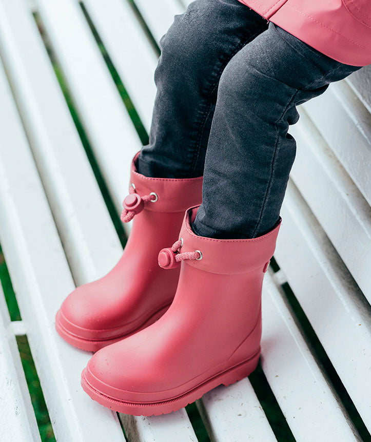 A pair of unisex short wellies by Igor, style Bimbi Euri, in raspberry pink with toggle fastening. Lifestyle image.