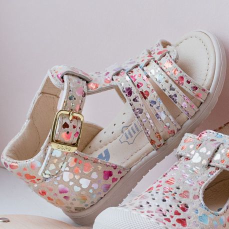 A girls open toe sandal by Bopy, style Reabou, in white with a multi colour foil  heart pattern. Buckle fastening around the ankle. Upright view.