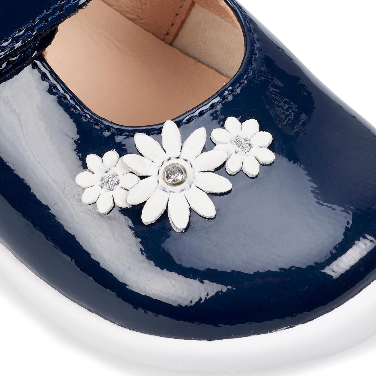 A girls Mary Jane shoe by Start-Rite, style Fairy Tale, in navy patent leather on white sole unit with white flower and diamante detail. Velcro fastening. Close up of flowers.