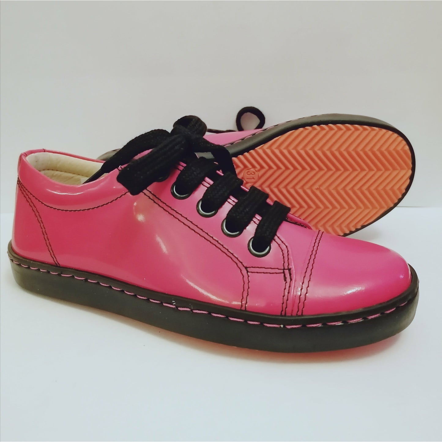 A girls shoe by Petasil, style Peel, in fuxia patent with black laces. Right side view, left view of orange and black sole.