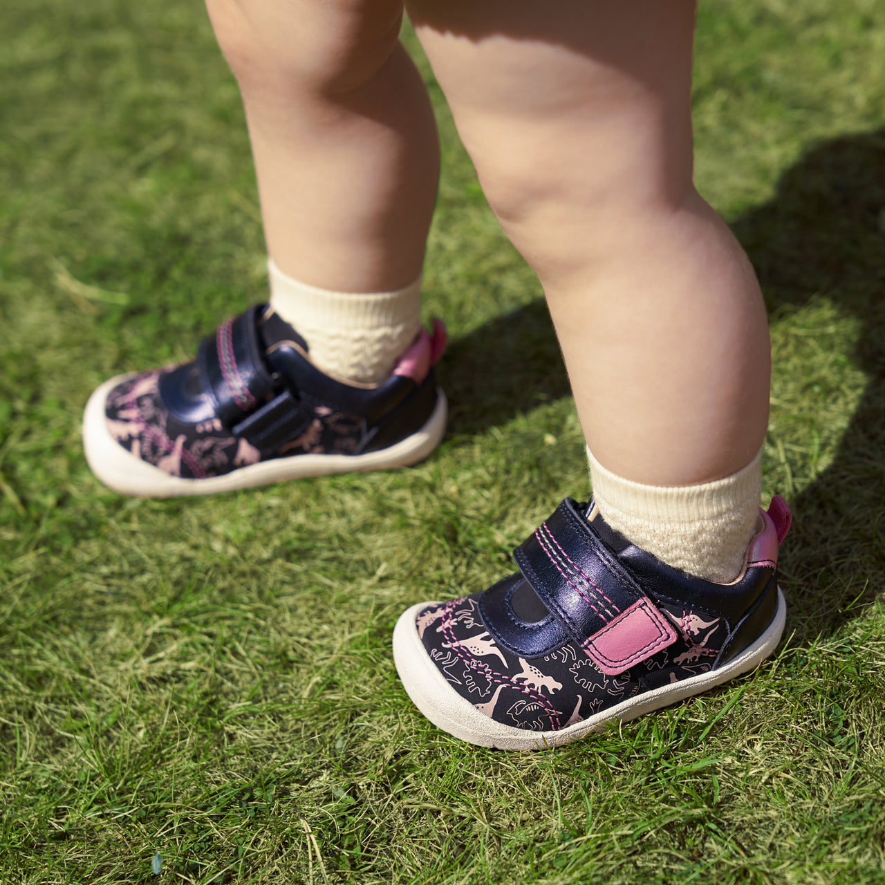  A girl wearing a pair of girls casual shoes by Start Rite, style Footprint, in navy and pink nubuck and leather with velcro fastening. Angled view.