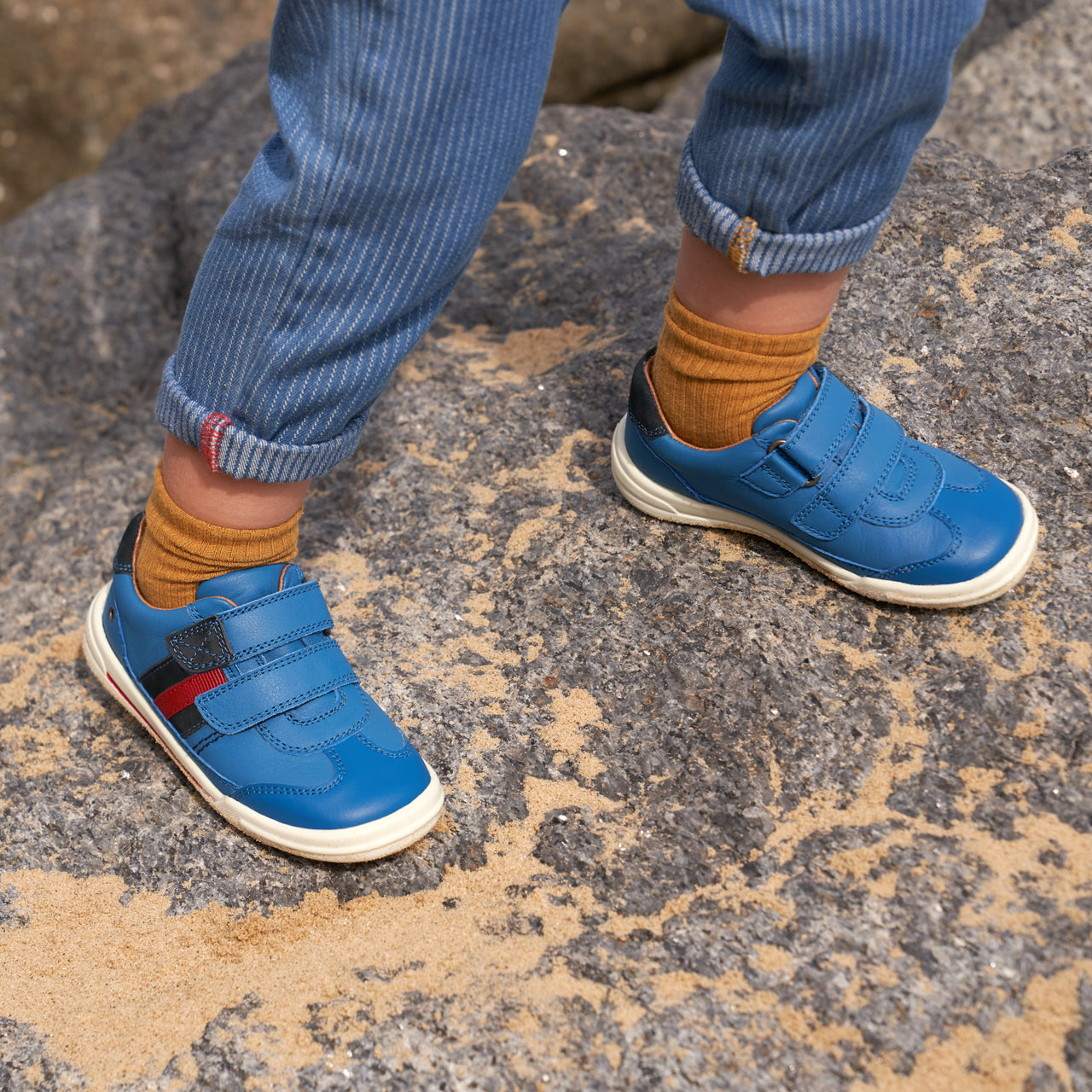 A child wearing a pair of boys casual shoes by Start Rite, style Seesaw, in blue and red leather with double velcro fastening Angled view.